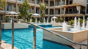 A hotel pool area with multiple fountains, palm trees, and umbrellas. - Near Eagle Beach| Top-Floor 1BR |Pool&Jacuzzi (Noord)