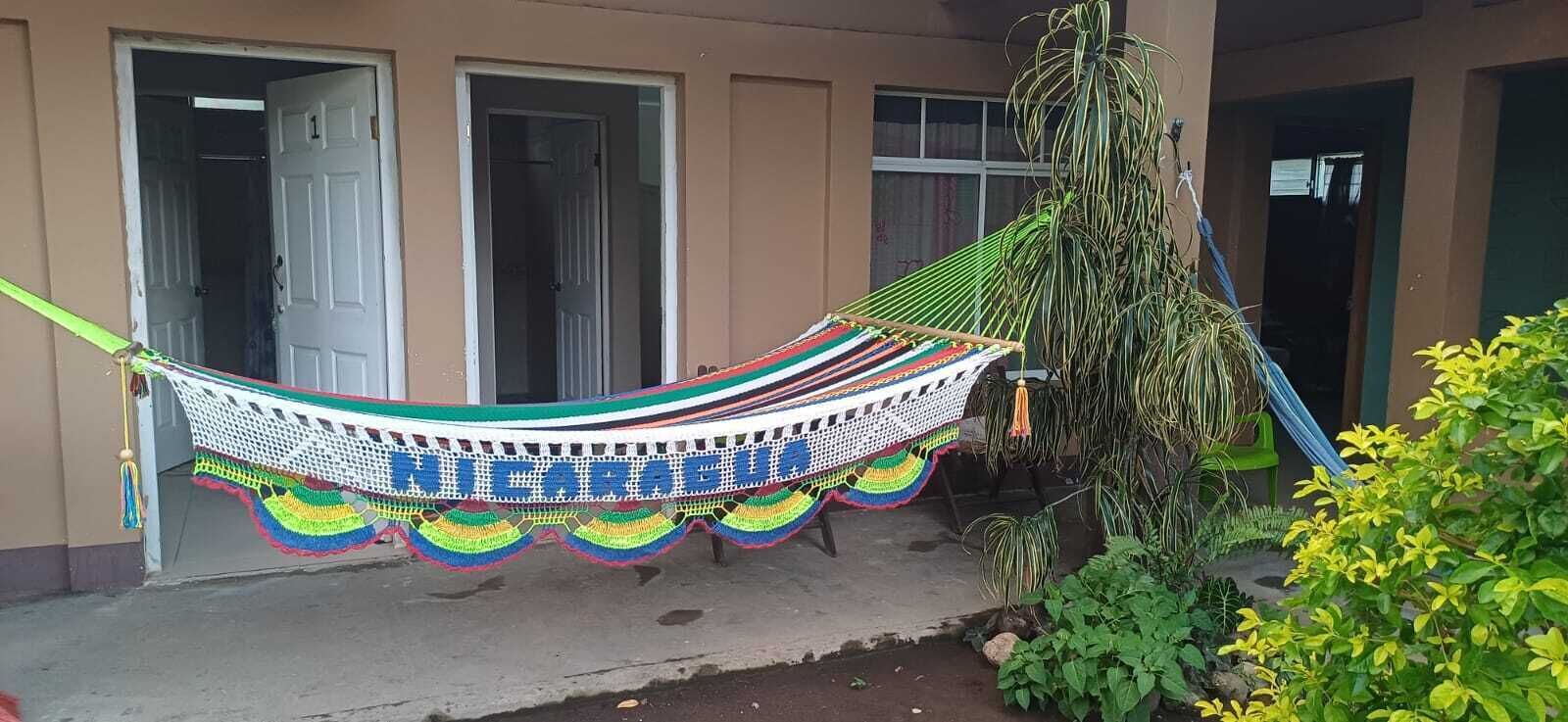 A hammock with a colorful crocheted edge, positioned in front of a building with a door and windows.