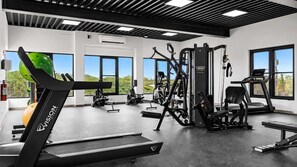 Une salle de sport équipée de matériel d’exercice, dotée de grandes fenêtres et offrant une vue sur la verdure.