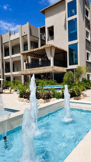 A hotel with a swimming pool, a thatched-roof structure, and a modern building with balconies. - Sunset Balconies | 5 minutes to Eagle Beach (Noord)