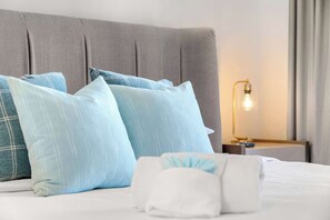 Ein ordentlich bezogenes Bett mit hellblauen und weißen Kissen, einem grauen Kopfteil und einer Nachttischlampe.