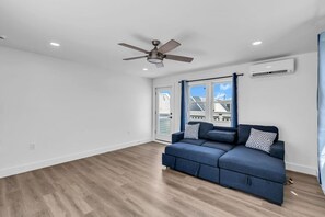 A room with a ceiling fan, a blue sofa with patterned cushions, wooden flooring, and a window with blinds. - Luxury Jersey Shore Retreat Rooftop Oasis & Beach (Seaside Heights)