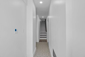 Ein schmaler, weiß getünchter Flur mit einem gemusterten Teppich, der zu einer Treppe führt.