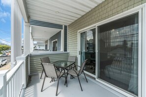 A covered outdoor patio with a table and chairs, a sliding glass door, and a view of the street. - Luxury Jersey Shore Retreat Rooftop Oasis & Beach (Seaside Heights)