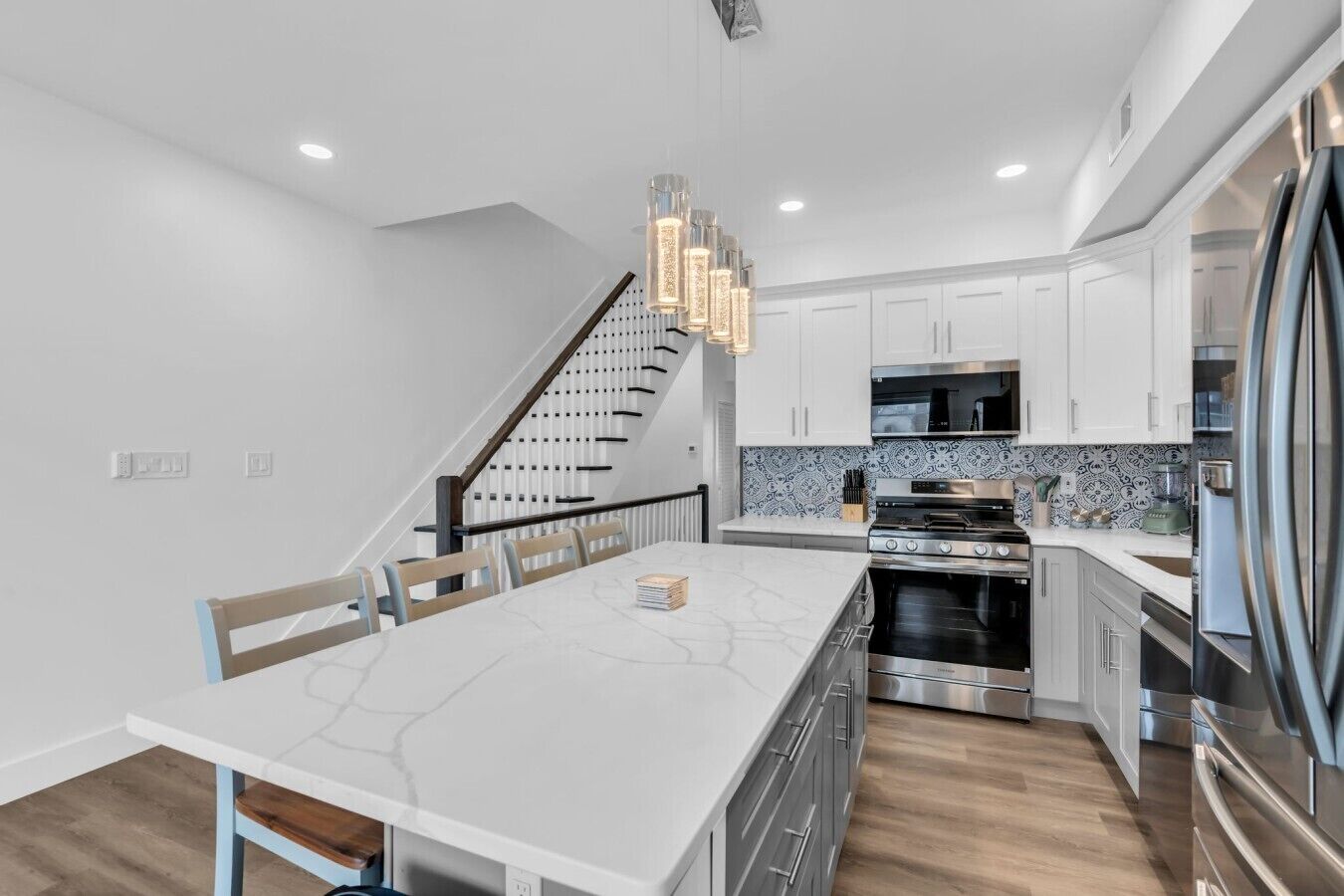 A modern kitchen with white cabinetry, a central island, stainless steel appliances, and a staircase leading to another level.