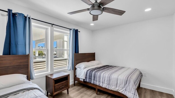 Een slaapkamer met twee bedden, een plafondventilator, een raam met gordijnen en uitzicht op de omgeving.