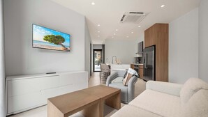 A modern living room with a flat-screen TV, a wooden coffee table, a grey sofa, and a kitchen area in the background. - 5-Min Drive to Eagle Beach|Large Patio|Pool&Jacuzzi (Noord)