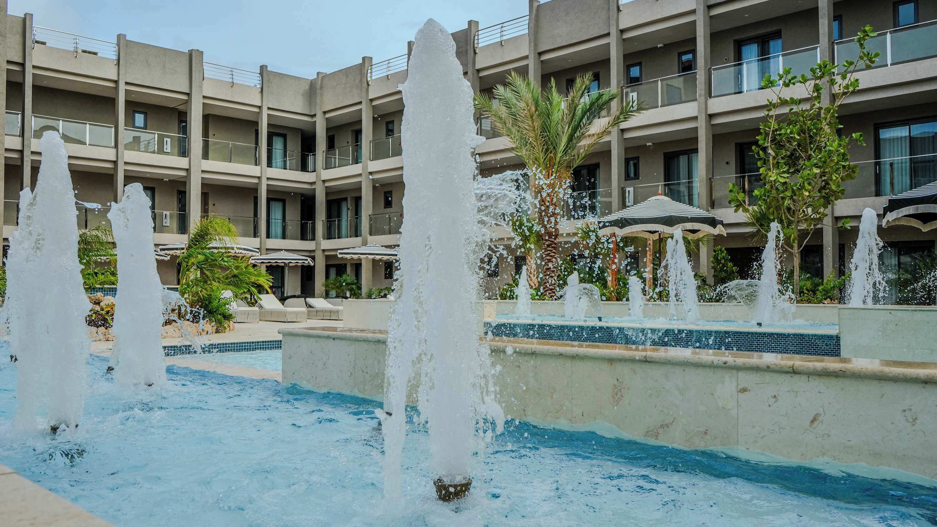 A hotel courtyard with multiple water fountains, a swimming pool, and a building with balconies.