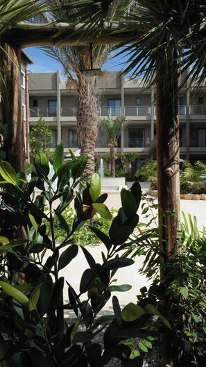 A courtyard with a palm tree, a fountain, and a building with balconies. - Top-Floor 1BR | Resort Pool | Close to Eagle Beach (Noord)