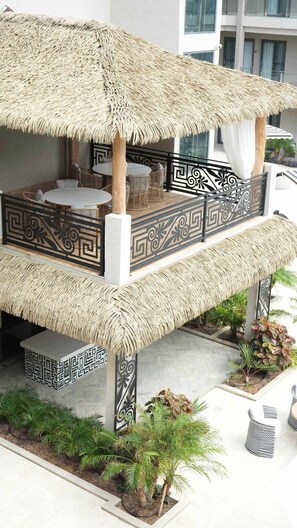 A thatched-roof outdoor seating area with a decorative railing, surrounded by potted plants. - Top-Floor 1BR | Resort Pool | Close to Eagle Beach (Noord)