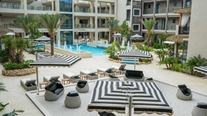 Ein Hotelpoolbereich mit Liegestühlen, Sonnenschirmen und einer Springbrunnenanlage in der Mitte.