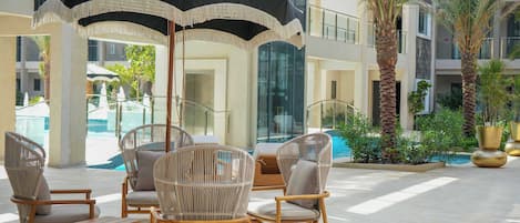 Un espace aménagé au bord de la piscine, avec des fauteuils en osier et une table, un grand parasol et un palmier.
