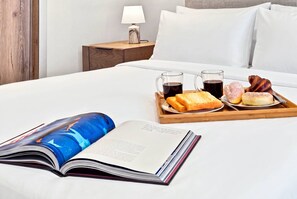 Un llit ben arrenjat amb un safata de menjars, un llibre i una tauleta de nit amb una làmpada.