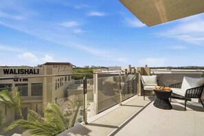 Ein Balkon mit Glastrennwand, Gartenmöbel und Blick auf ein Gebäude mit der Aufschrift 'WALISHALI'.