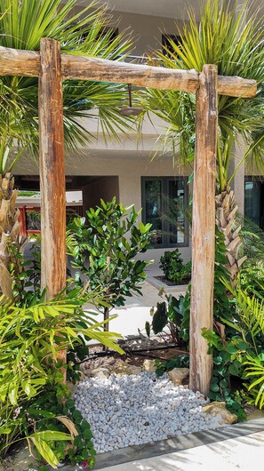 A wooden pergola structure surrounded by lush greenery and white pebbles. - Sunrise & Sunset | Corner 1BR | Near Eagle Beach (Noord)