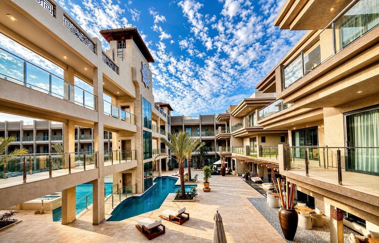 A hotel atrium with a central pool, multiple balconies, and a clear sky.