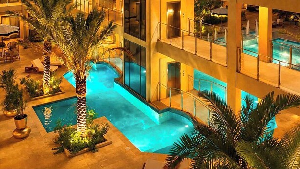 A multi-story hotel with a central swimming pool, balconies, and a decorative light feature on the facade. - Top-Floor 1BR | Close to Aruba’s Best Beaches (Noord)
