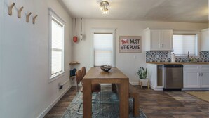 A modern kitchen with white cabinets, a wooden dining table, and a kitchen island. - Oasis Dream: Pet-Friendly Hot Tub, Cold Plunge, EV Charger & Stargazing (Twentynine Palms)