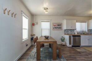 A modern kitchen with white cabinets, a wooden dining table, and a kitchen island. - Oasis Dream: Pet-Friendly Hot Tub, Cold Plunge, EV Charger & Stargazing (Twentynine Palms)