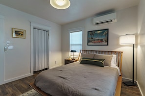 Un dormitorio con cama, mesita de noche, lámpara, aire acondicionado y un cuadro en la pared.