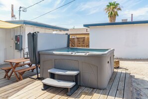 A hot tub with steps, a wooden table, and a bench on a wooden deck.