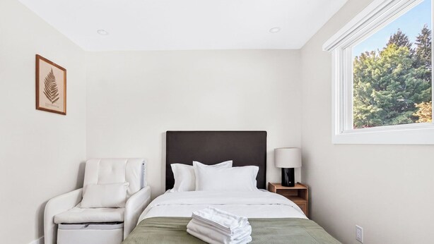 Habitación de hotel con cama, una silla, una mesita de noche y una ventana con vistas a árboles.