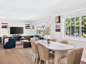 A modern living room with a flat-screen TV, a sofa, a dining table with chairs, and a large window with a view of the outside. - Newly renovated 6-bedroom 6BA house with AC in central Vancouver (Vancouver)