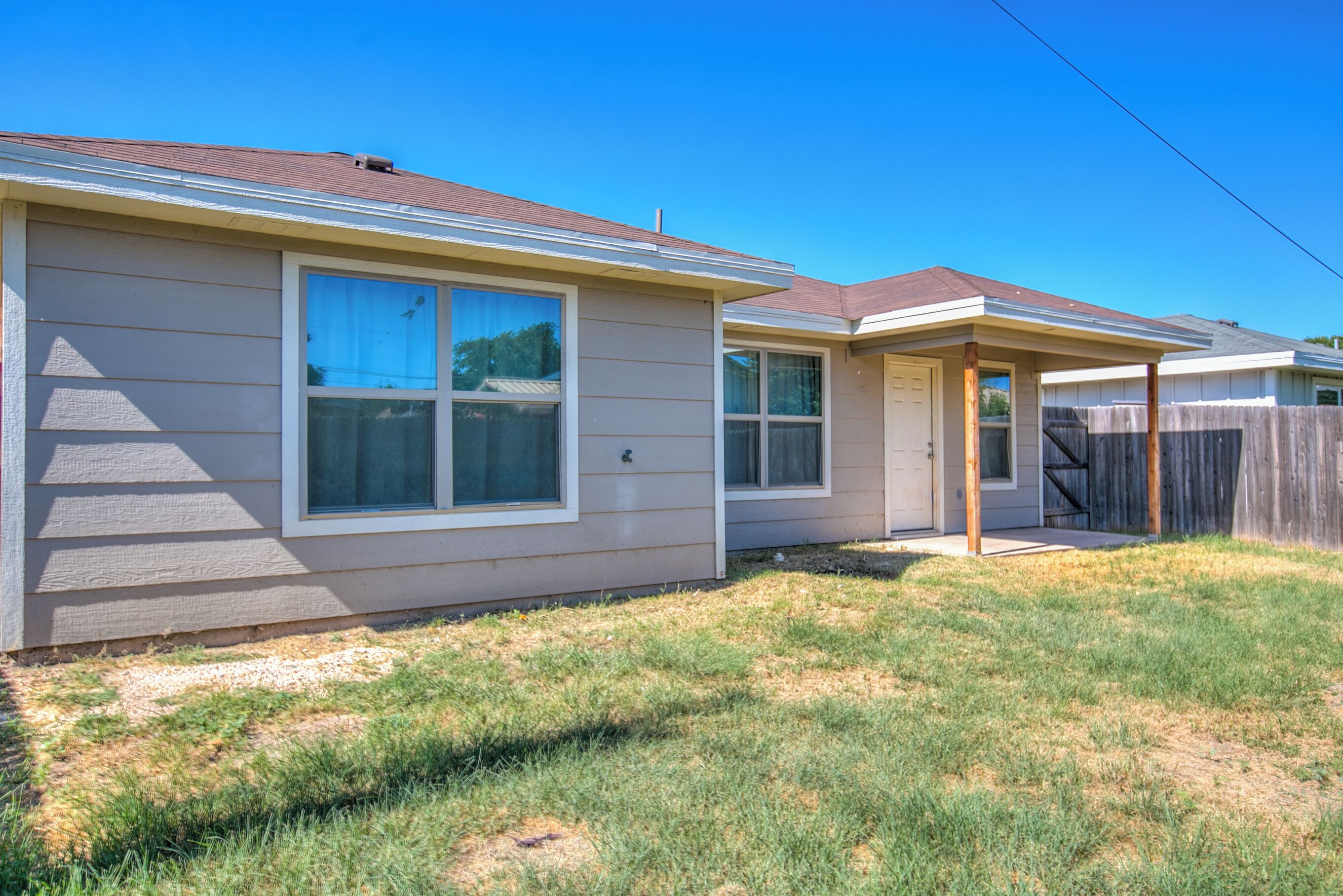 A single-story residential house with a front porch, a garage, and a fenced backyard.