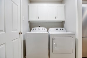 A laundry room with two stacked washers and dryers, white cabinets above, and a white door on the left. - Riverside Retreat 3BDRM/2BA (San Angelo)