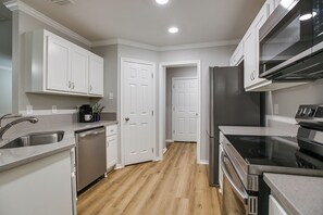 A modern kitchen with white cabinetry, stainless steel appliances, and a wooden floor. - Riverside Retreat 3BDRM/2BA (San Angelo)