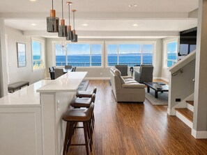 Een moderne keuken met een centraal kookeiland, barkrukken en uitzicht op zee.