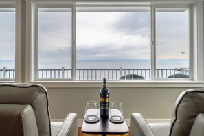 Een kamer met uitzicht op de zee door een groot raam, een tafel met een fles en glazen, en twee stoelen.