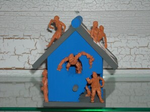 A toy house with figures on top and a figure standing in front.