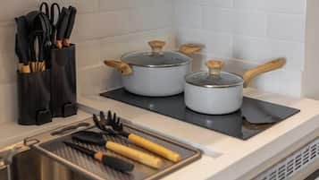 Uma cozinha com duas panelas em um fogão por indução preto, uma tábua de corte com utensílios, e um suporte preto para talheres com facas.