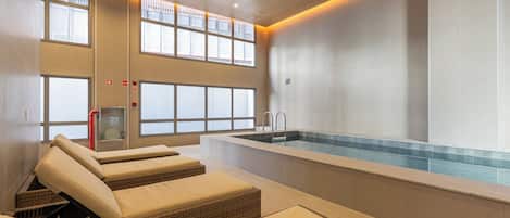 A spa area with a pool, loungers, and large windows.