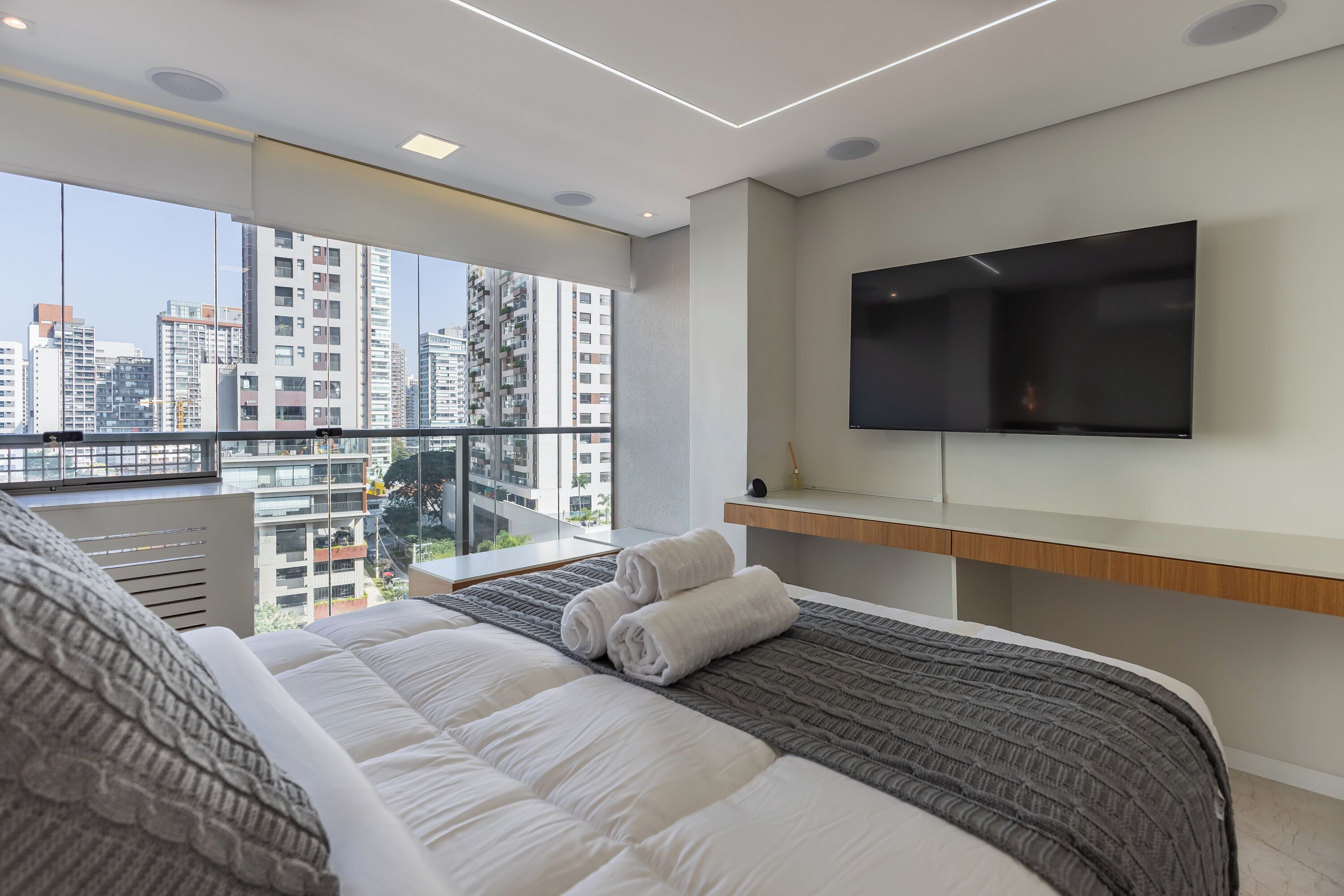 A modern hotel room with a large bed, a mounted TV, and a balcony with a city view.