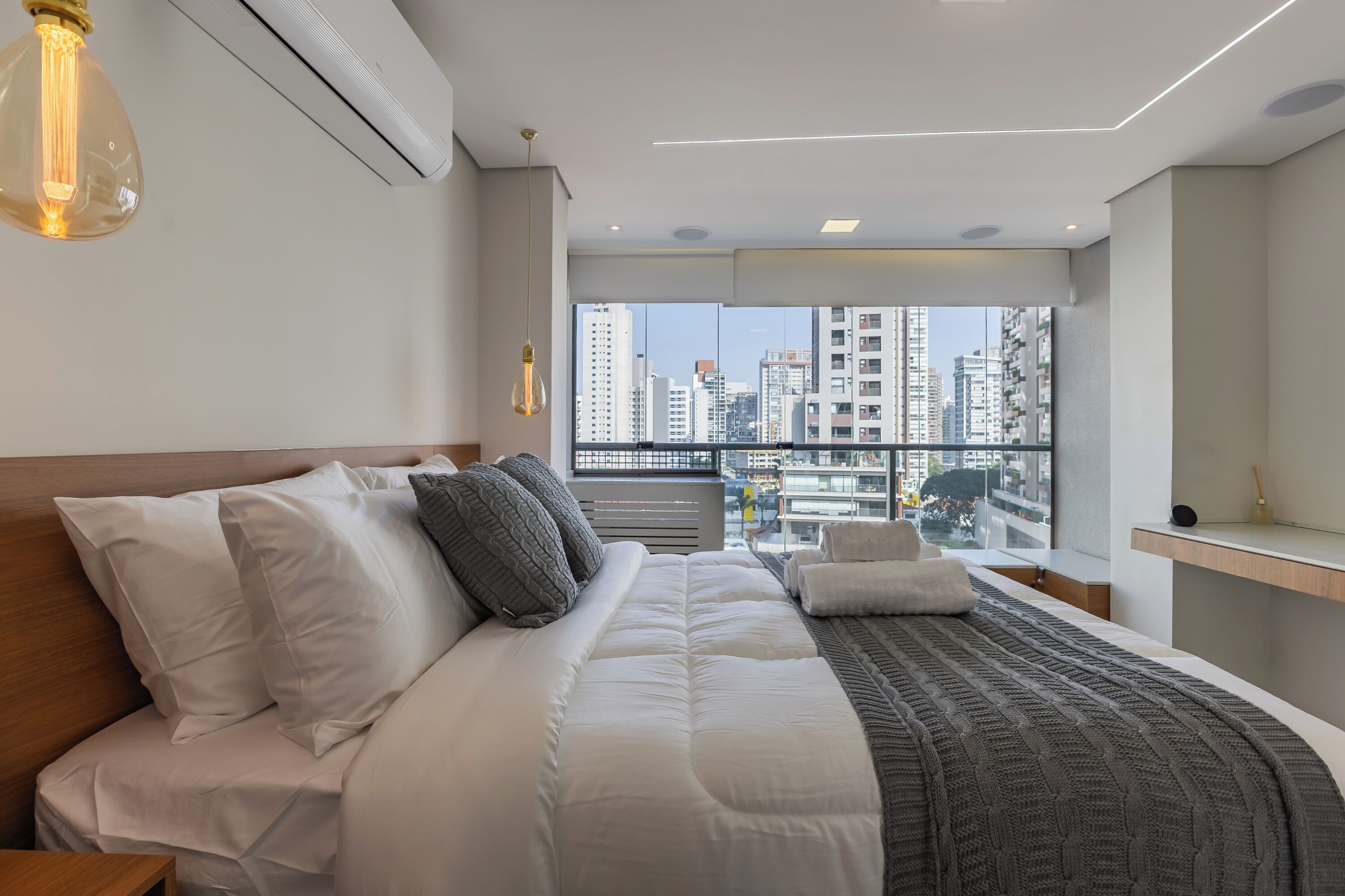 A modern hotel room with a large bed, a view of the city through floor-to-ceiling windows, and a minimalist design.