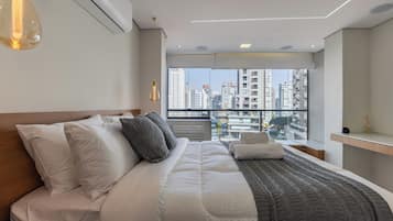 A modern hotel room with a large bed, a view of the city through floor-to-ceiling windows, and a minimalist design.
