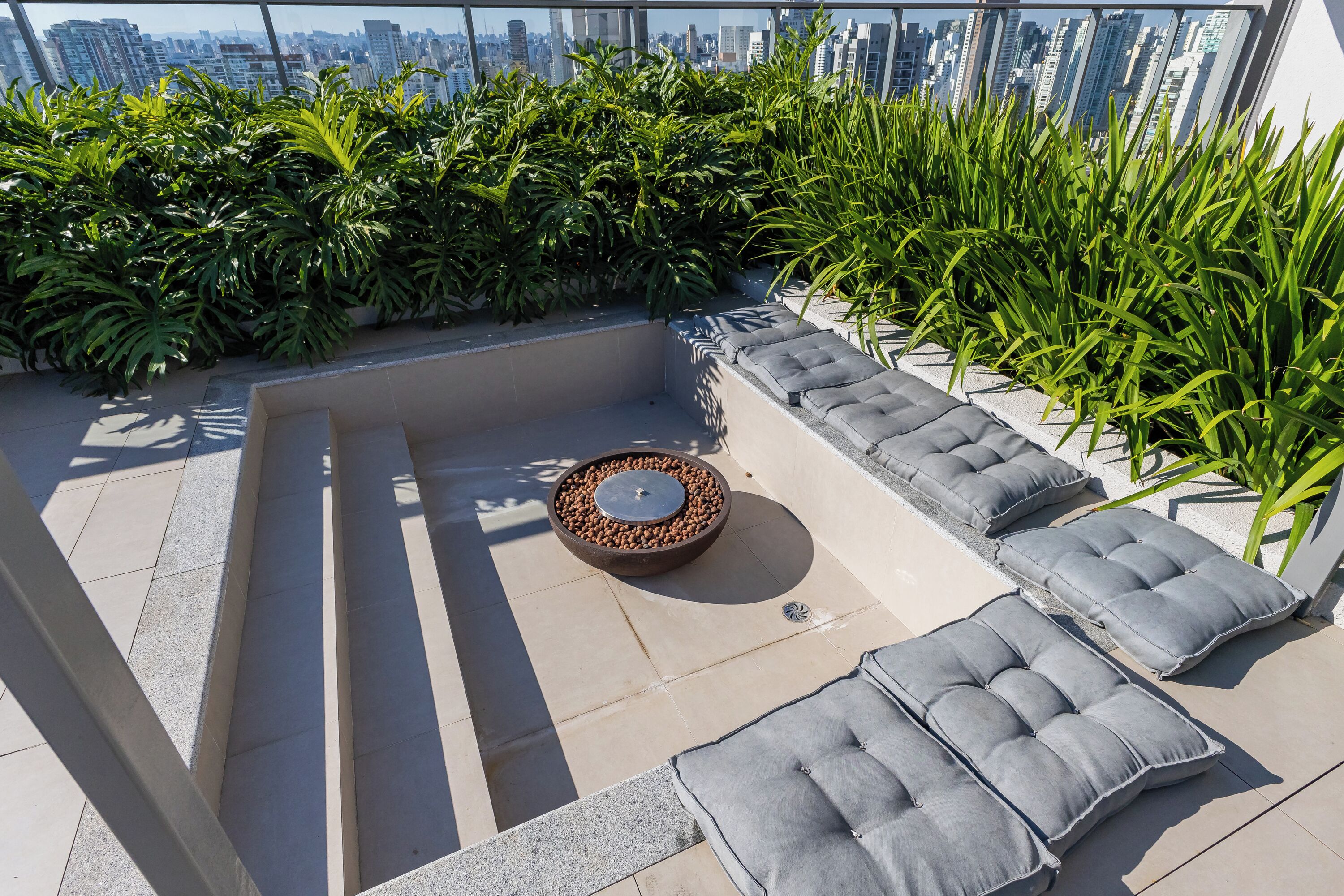 A rooftop terrace with a seating area, a fire pit, and a view of the city skyline.