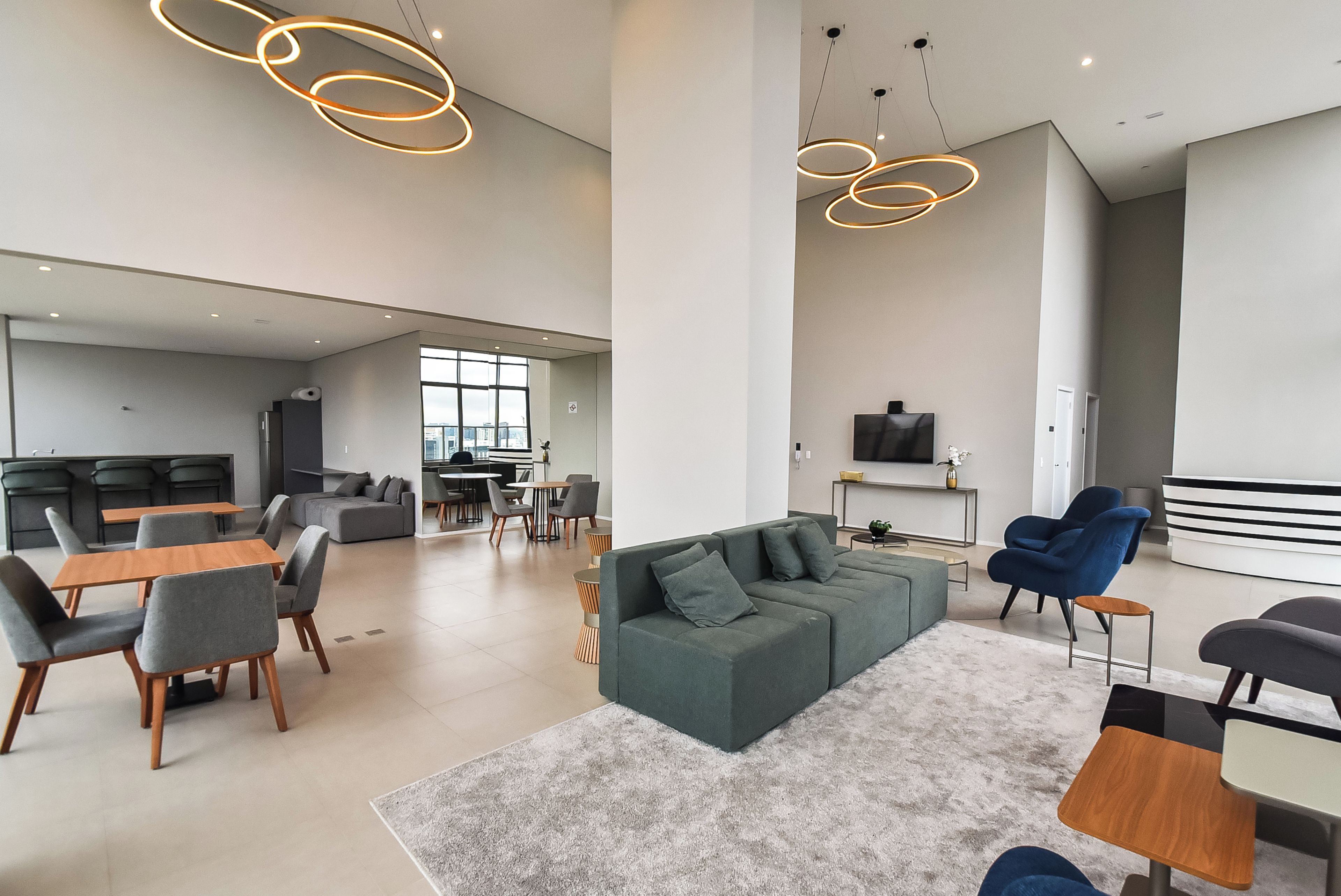 A spacious living area with a large sofa, dining table, and chairs, a kitchen in the background, and modern pendant lighting.