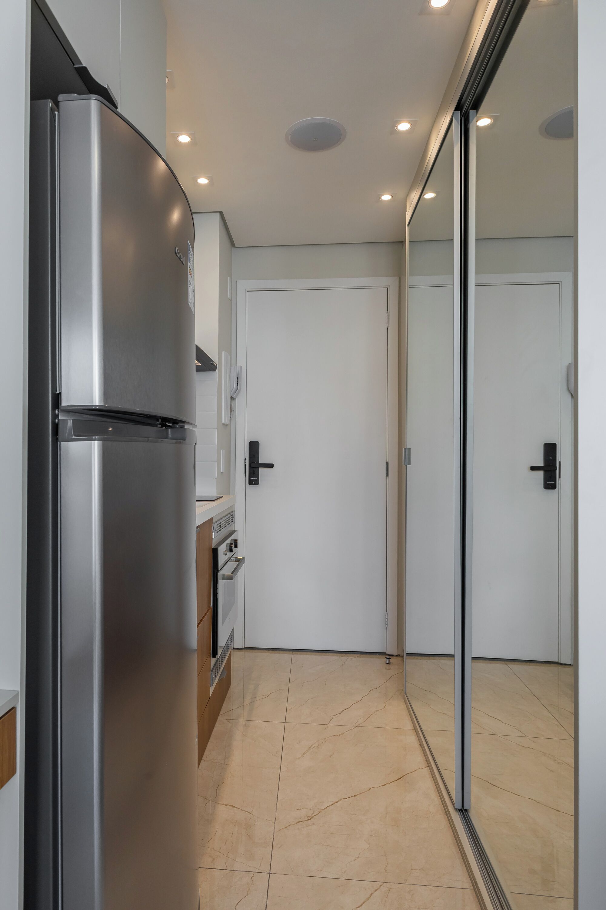 A modern kitchen with a stainless steel refrigerator, a built-in oven, and a white door.