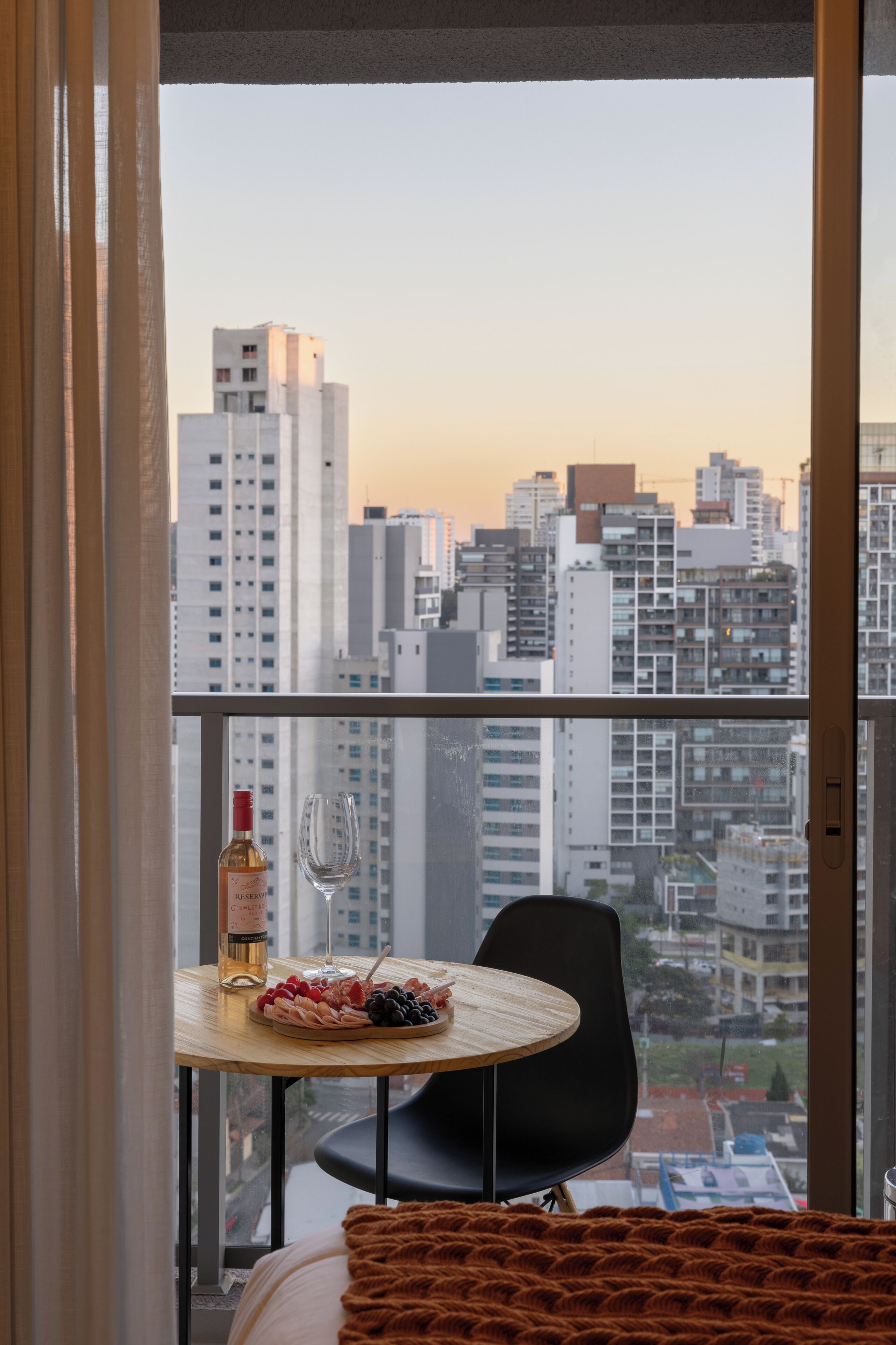 A high-rise apartment with a city view, a dining table with a bottle and a glass, and a chair.