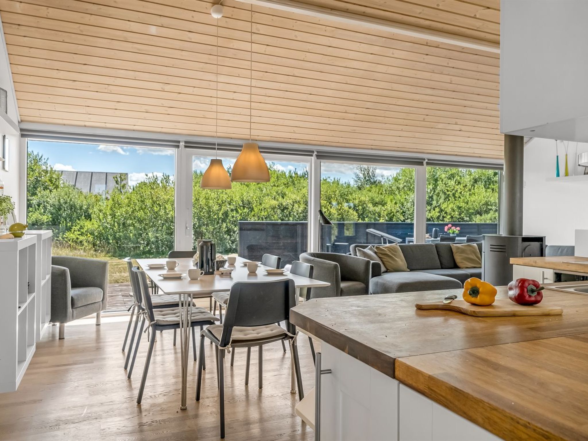 A modern kitchen with a wooden ceiling, large windows, and a dining area with a sofa and chairs.