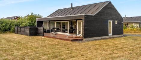A modern house with a large deck, a covered outdoor seating area, and a well-maintained lawn.