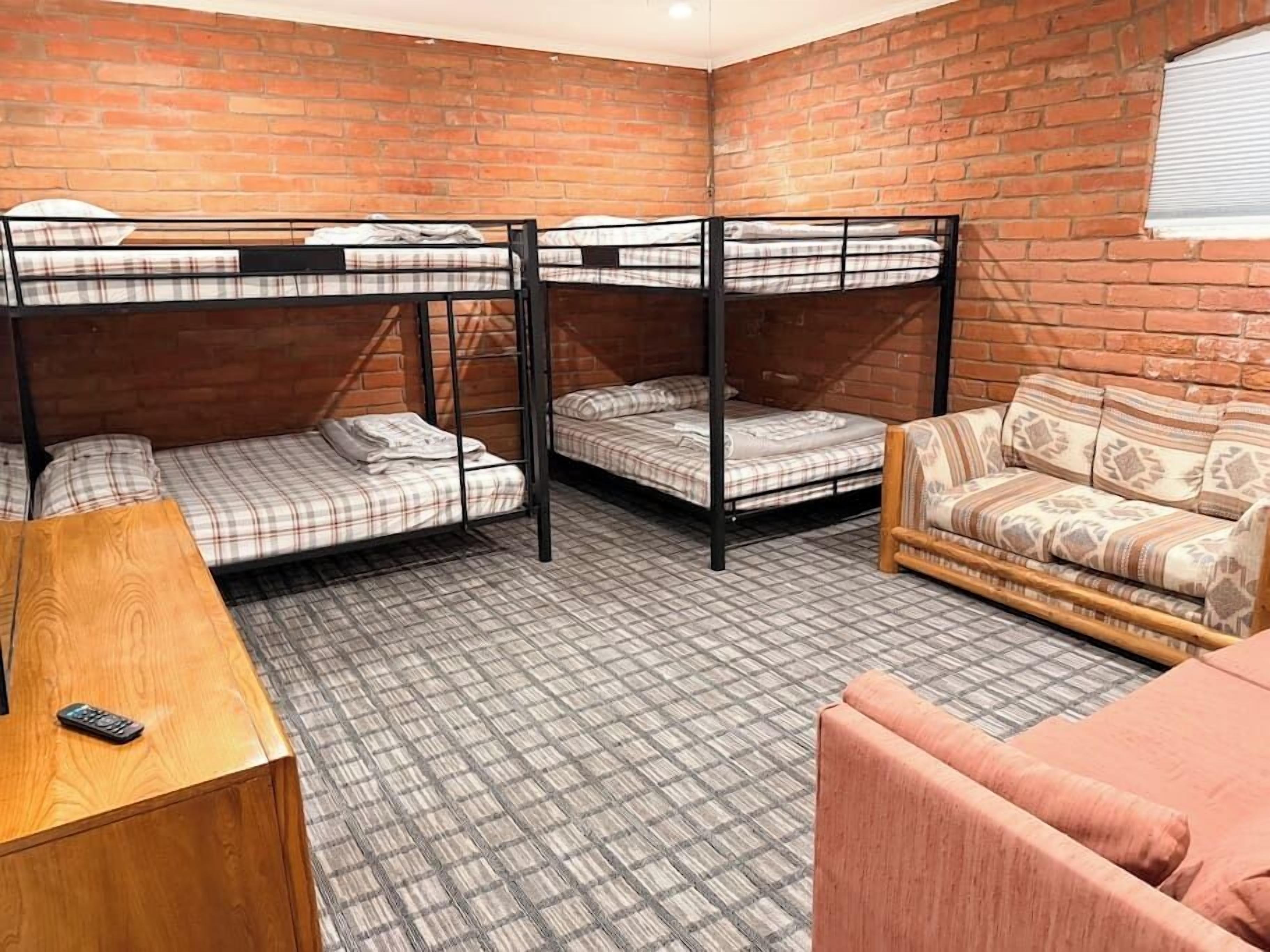 Una habitación con tres literas, un sofá, una mesa de madera y una alfombra estampada.