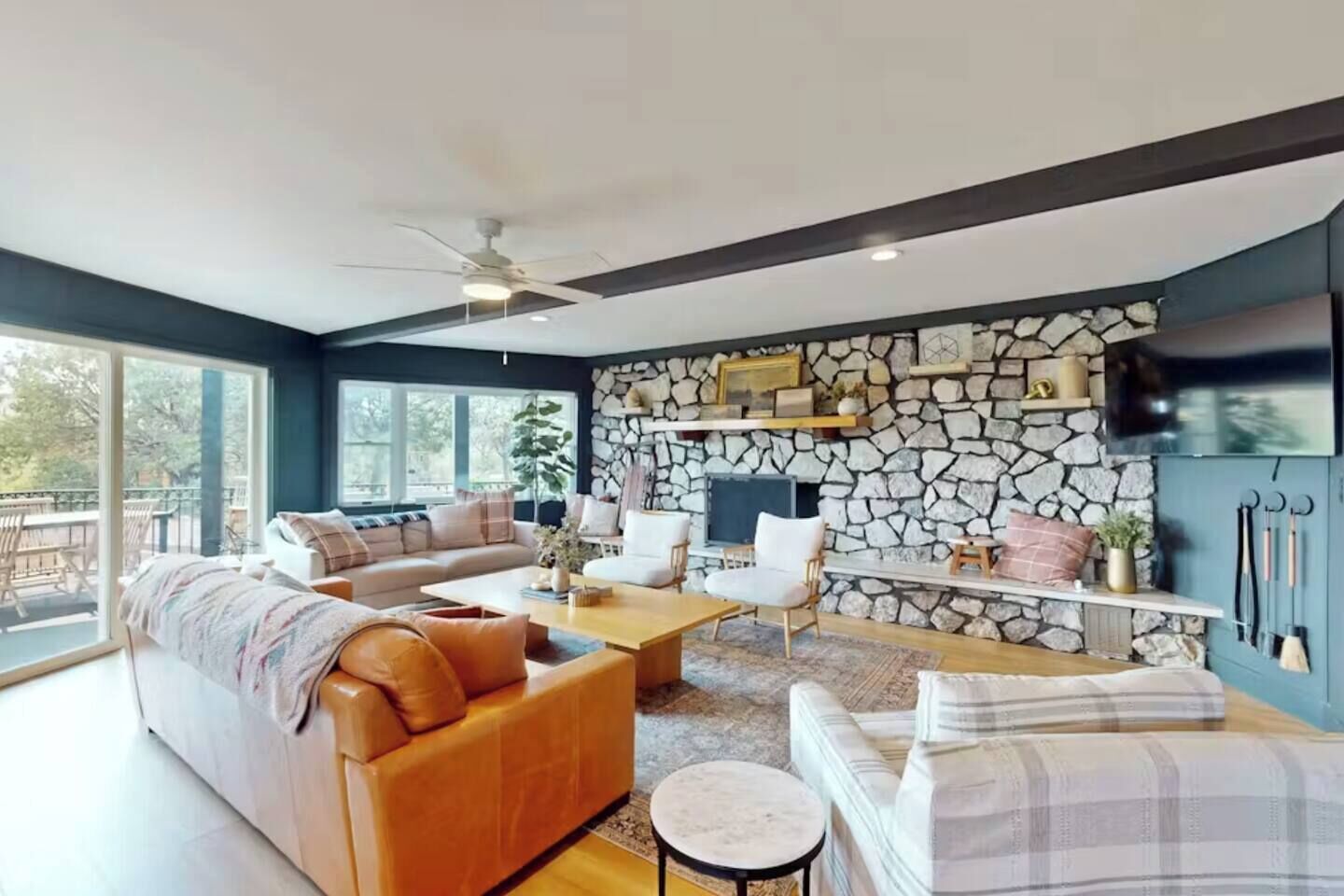 A modern living room with a stone wall, a fireplace, and a large window overlooking a deck.