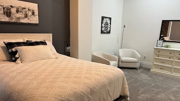 Une chambre à coucher avec un grand lit, une chaise, une commode et un tableau accroché au mur.