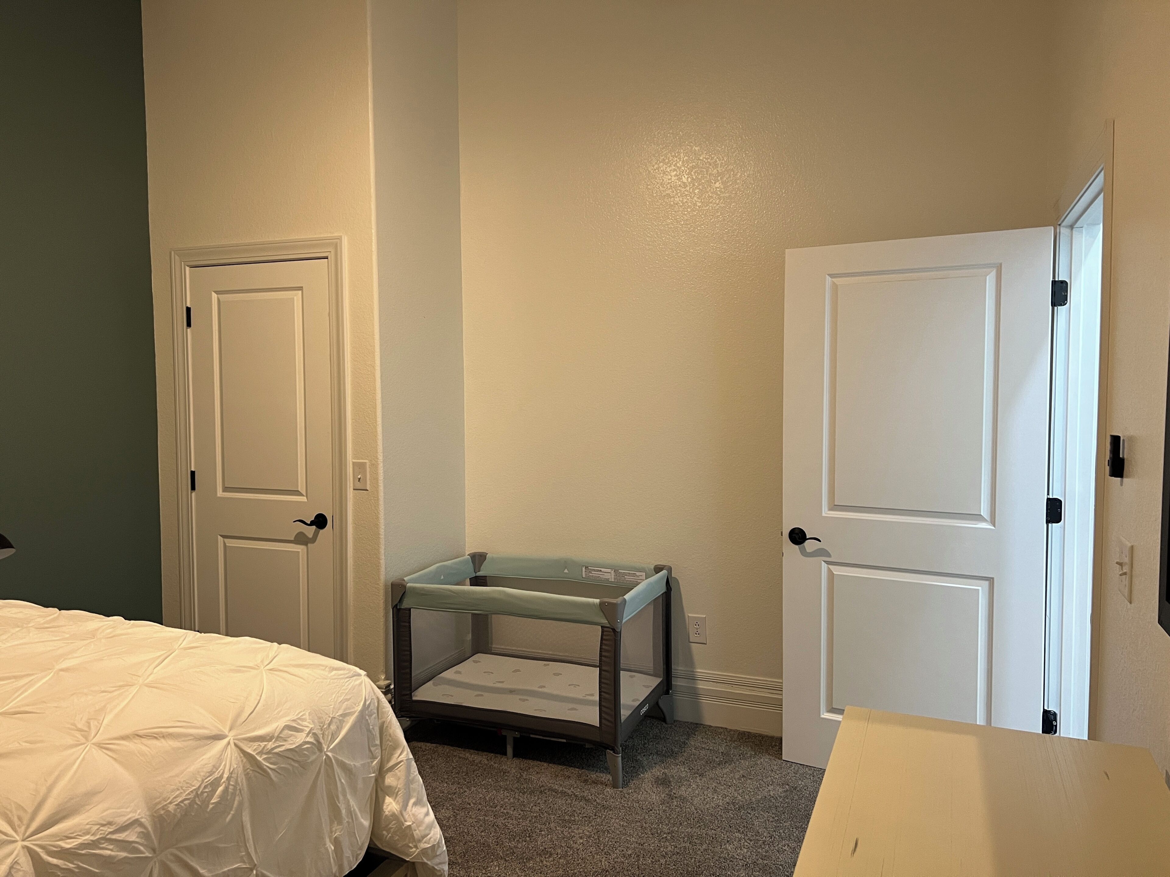 Un dormitorio con dos puertas, una cama con cubrecama blanco y una mesita de noche con tapa azul claro.