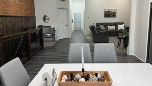 A modern living room with a sofa, a dining table with chairs, a fireplace, and a hallway leading to another room. - Adorable 2-bedroom apartment with jetted Jacuzzi tub adjacent to Coffee Shop! (Brookfield)