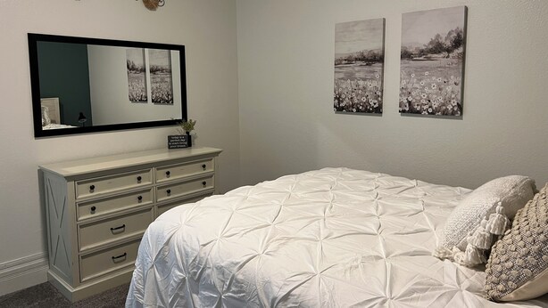 A bedroom with a bed, dresser, mirror, and two framed pictures on the wall. - Adorable 2-bedroom apartment with jetted Jacuzzi tub adjacent to Coffee Shop! (Brookfield)